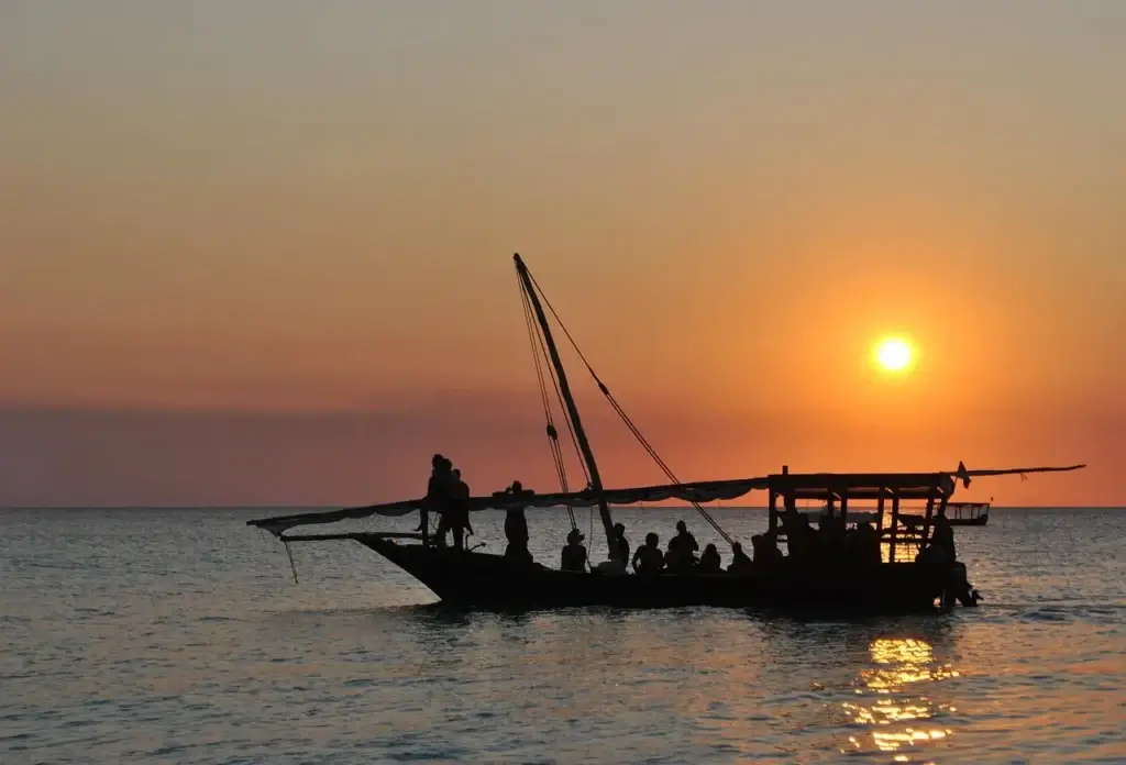 27 Things to Do in Zanzibar (2026 Must‑See List) 2 Traditional dhow boat sailing at sunset on a Zanzibar beach with an orange sky and calm ocean.