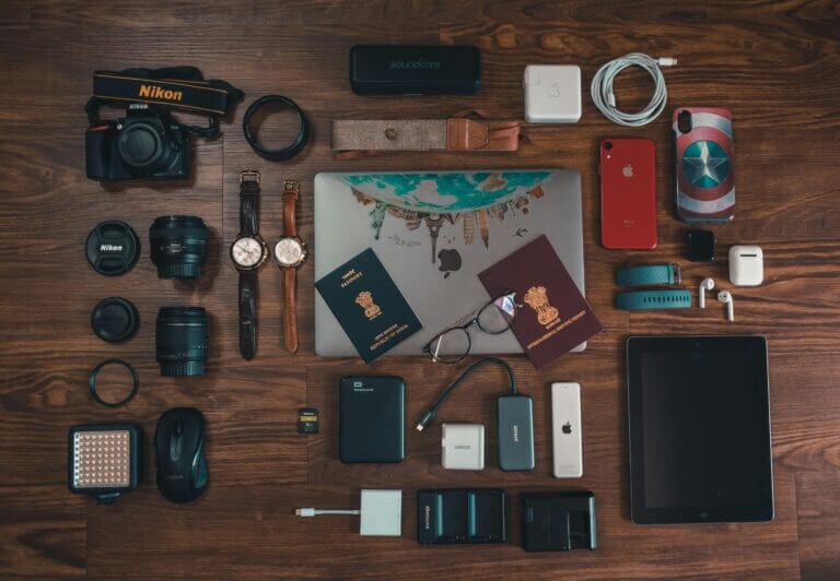 Flat lay of essential safari packing gear including binoculars, neutral-colored clothing, a wide-brimmed hat, and a telephoto camera lens.