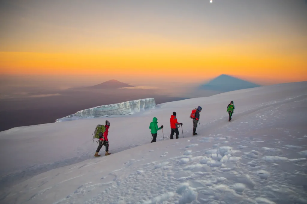 Hikers trekking up Mount Kilimanjaro with porters carrying gear, showing the full mountain crew required for climbing